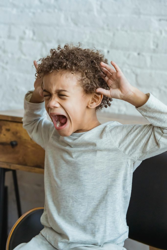Young black child showing frustration in an indoor setting, hands on head in distress.